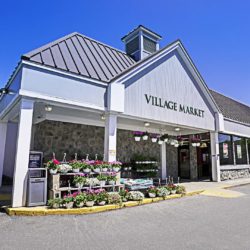 Front of grey building with Village Market sign and flower out front